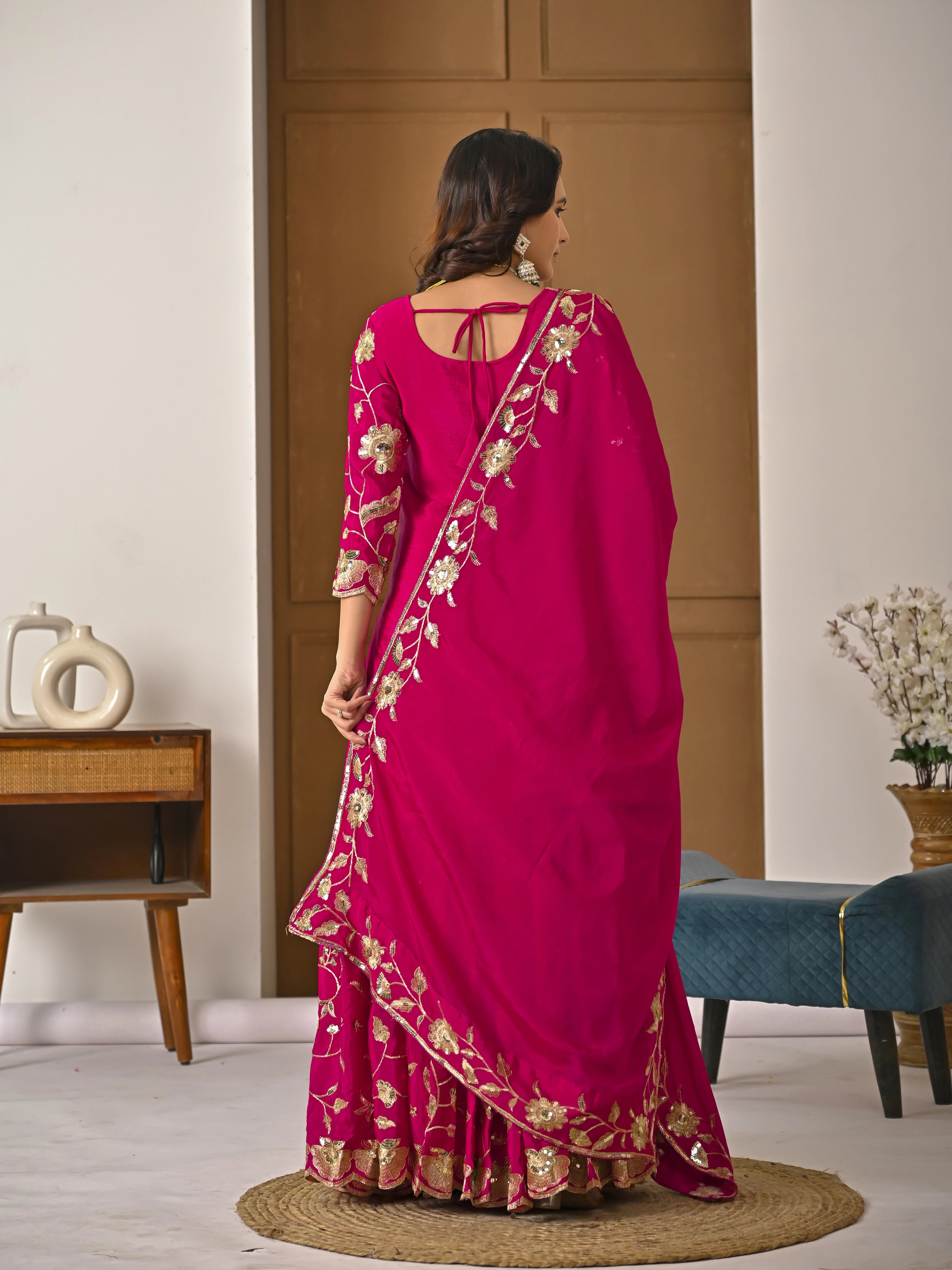 Woman wearing a pink saree with gold patterns in a room setting.